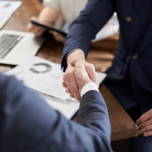 Two people shaking hands across a desk after a meeting