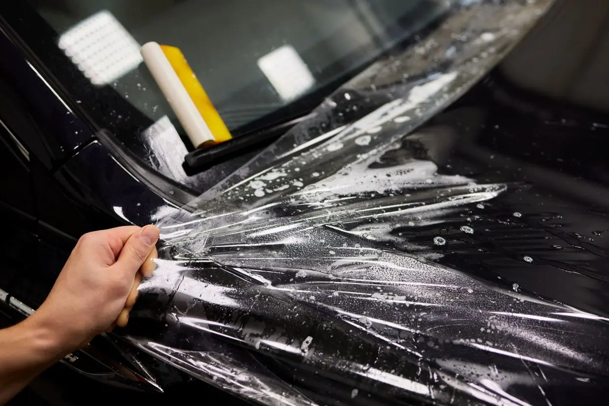 Clear protective film being smoothed onto a black car hood