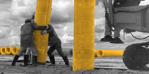 Workers guiding a pile into position with a rig behind them